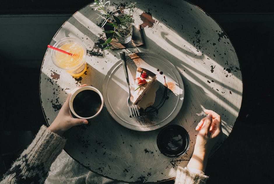 Overhead view of a cozy café table with a slice of cake, coffee, and juice, bathed in warm afternoon light
