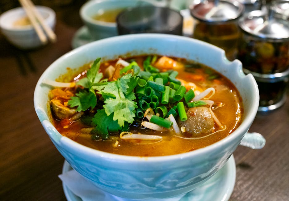 A flavorful Thai Tom Yum soup garnished with fresh herbs served in a ceramic bowl