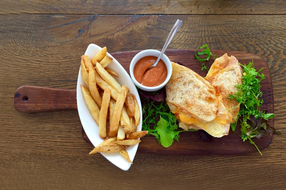 Delicious grilled cheese sandwich with crispy fries and a side of dipping sauce on a wooden table